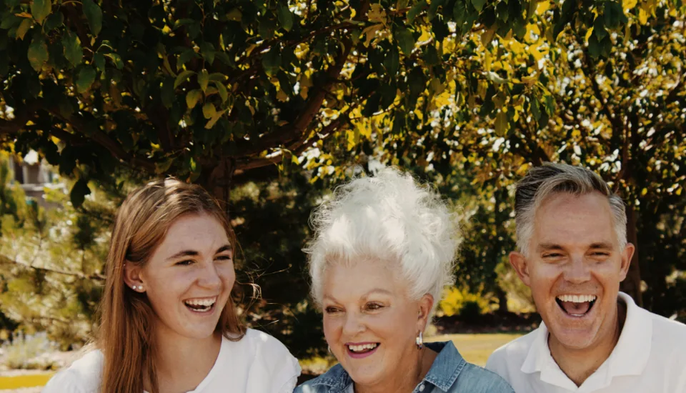 An older woman outdoors with her two grown children, all laughing