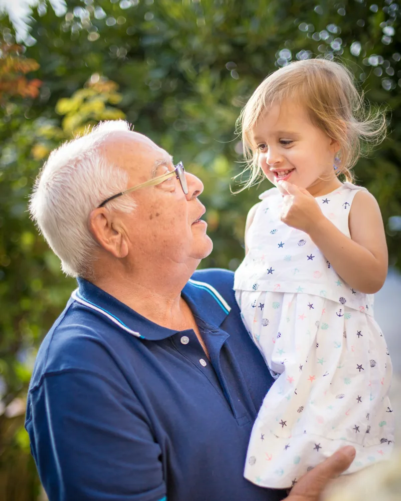 A man in his seventies holding his laughing granddaughter